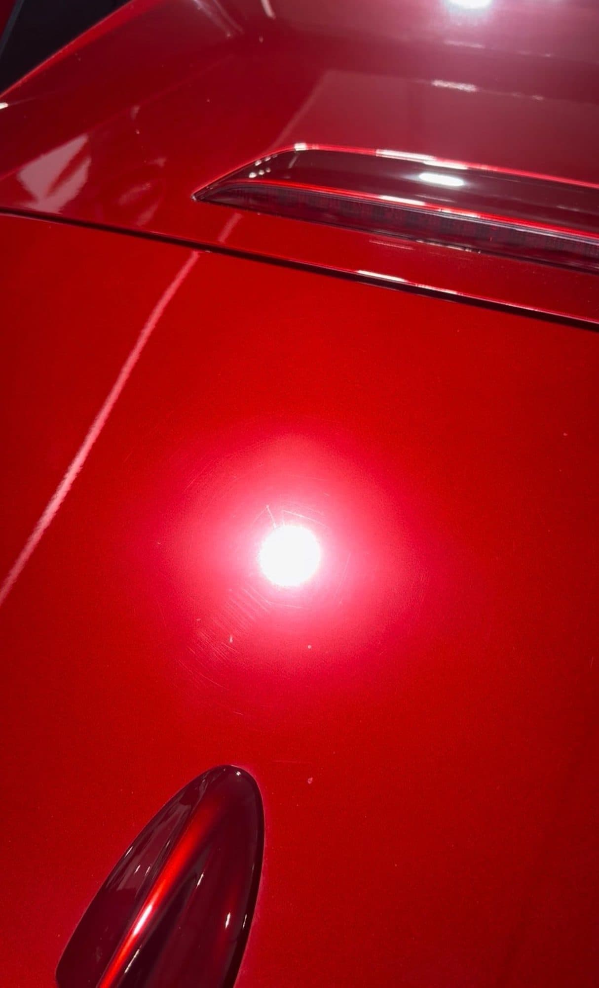 Red paint before correction, with swirl marks under a light