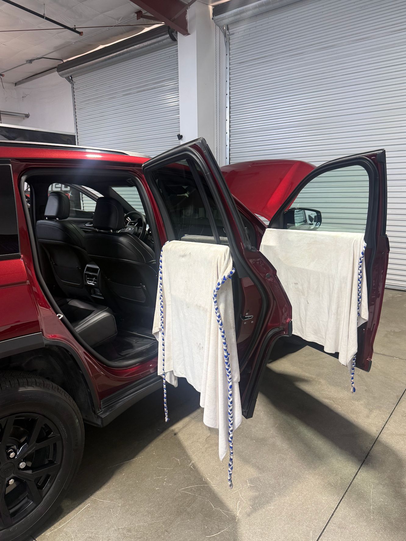 Red Jeep Grand Cherokee in the shop with doors open and door panels covered in towels during window tint prep
