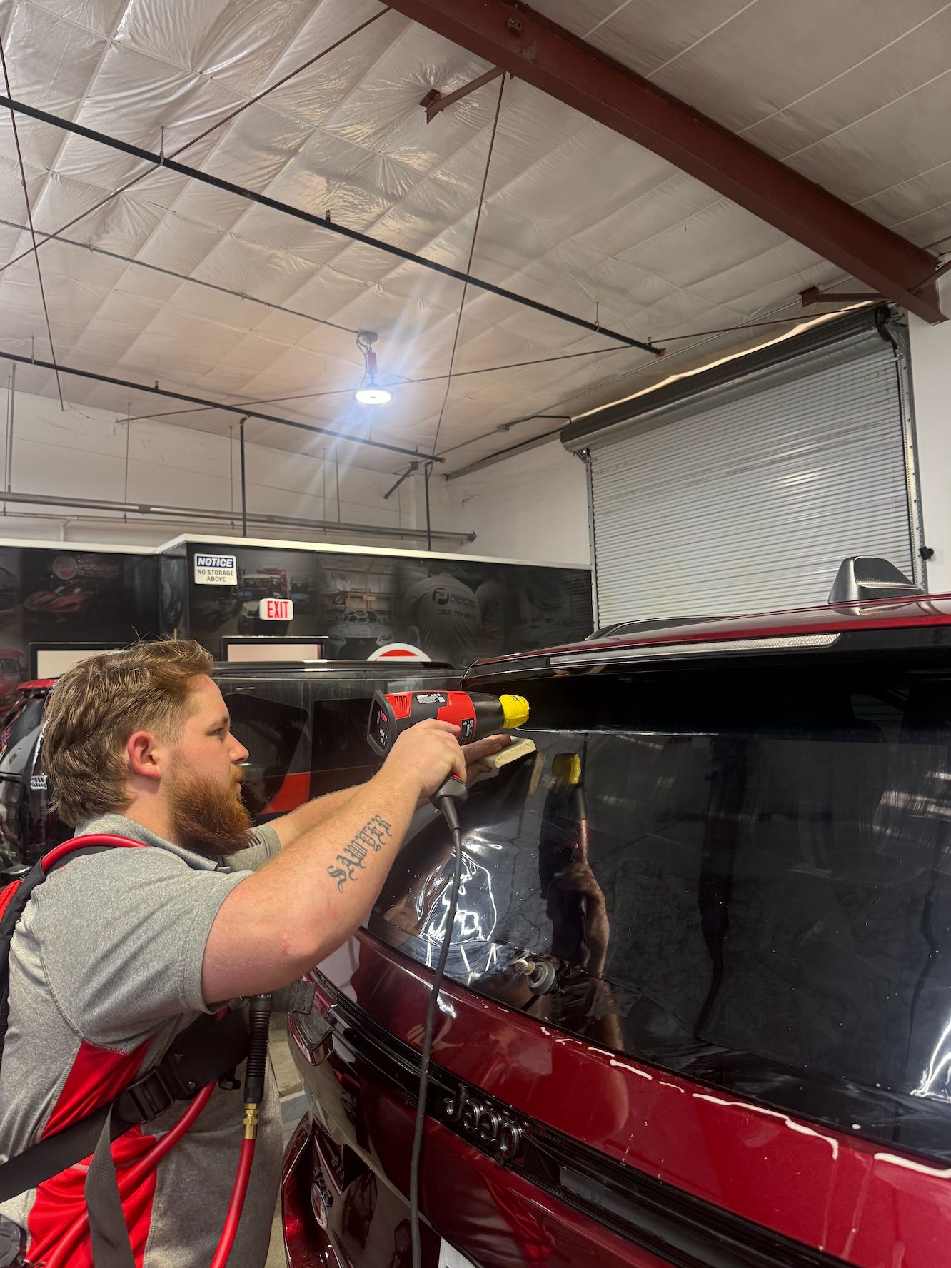 Installer using a spray bottle on the rear glass of a red Jeep Grand Cherokee before applying window tint