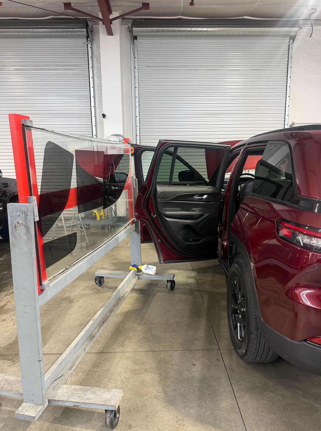 Window tint film on a rolling glass rack next to a red Jeep Grand Cherokee with its rear door open