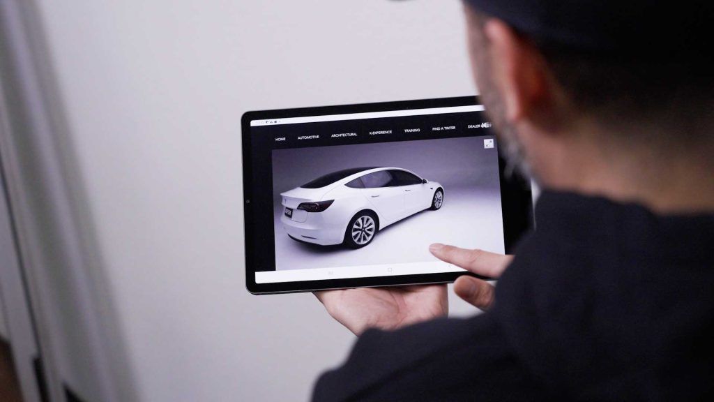 A person holding a tablet displaying a white Tesla car on a website.